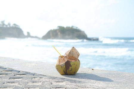 A fresh coconut with a straw sits on a stone surfaceの写真素材
