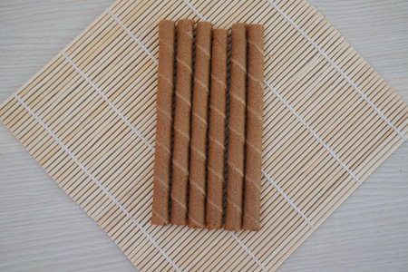 Six chocolate wafer rolls are neatly arranged in a row on a bamboo matの写真素材