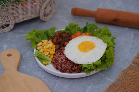 A vibrant meal consisting of red rice, meat, corn, carrots, lettuce, and a sunny side up eggの写真素材
