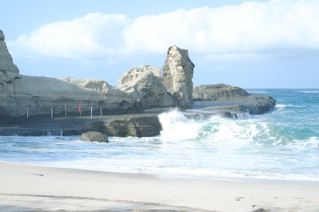 Waves crash against the rugged rock formations on a pristine beach under a bright blue skyの写真素材