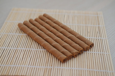 Six chocolate wafer rolls are neatly arranged in a row on a bamboo matの写真素材