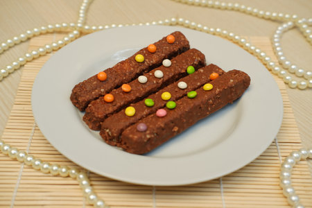 On a smooth, light wooden surface, a white round plate holds several chocolate coated snack barsの写真素材
