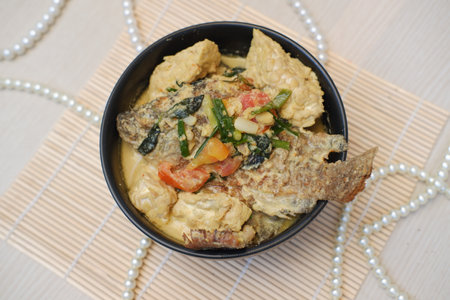 The dish appears to be a rich and creamy coconut milk based curry, featuring a whole fried fish as the centerpieceの写真素材