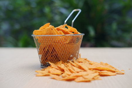 The image shows a small wire mesh basket filled with crispy, triangular corn chips, commonly known as nachos or tortilla chipsの写真素材