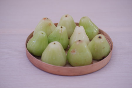 a round wooden tray filled with fresh, light green wax apples, also known as water apples or Syzygium samarangenseの写真素材