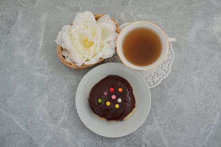 It features a white plate holding a donut topped with a rich chocolate glaze and decorated with colorful candy dotsの写真素材