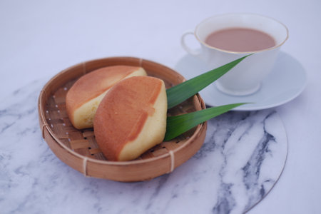In a round bamboo tray, there are two golden-brown pancakes or soft sponge cakes, likely traditional Indonesian snacks known as kue apem or kue dorayakiの写真素材