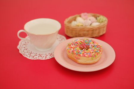 a pink plate holding a donut topped with bright pink icing and a generous amount of colorful sprinklesの写真素材