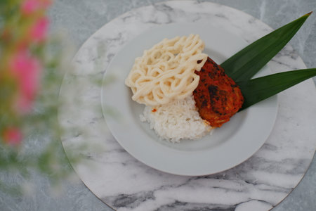 The dish includes a portion of white steamed rice, a piece of grilled or roasted chicken coated in a spicy red seasoningの写真素材