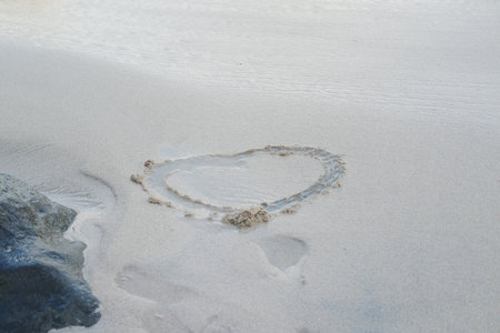 Drawn in the wet sand is the shape of a heart, partially filled with a thin layer of water from the receding wavesの写真素材