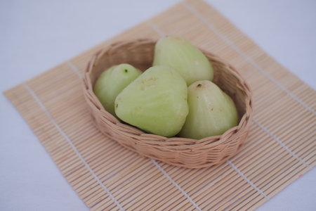 a small woven basket containing four light green fruits placed on a bamboo matの写真素材