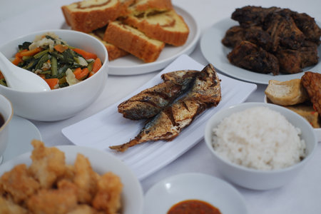 a delicious and diverse Indonesian meal spread. At the center is a plate of two fried mackerel fish, golden and crispyの写真素材