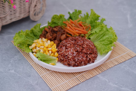 Healthy and balanced meal with red rice, chicken, and fresh vegetables.の写真素材