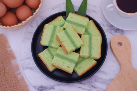 Delicious layered pandan cake slices on a black plate with eggs and coffeeの写真素材