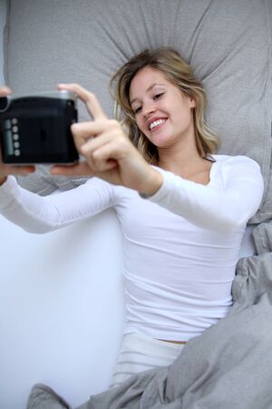 Cute blond woman takes a selfie in bedの写真素材