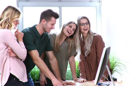Group of people laughs while using a computer at the office