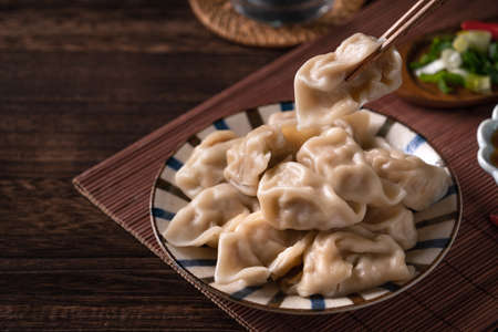 Eating fresh, delicious boiled dumplings, jiaozi on wooden table background with soy sauceの写真素材