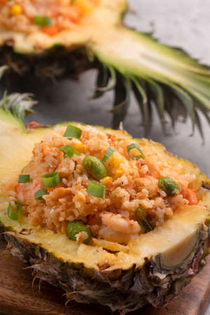 Delicious carved pineapple served as a bowl container boat stuffed with fresh pineapple tomato sauced seafood fried rice.の写真素材
