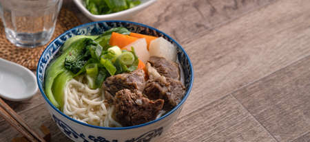 Beef noodle soup. Close up of Taiwanese famous food with sliced braised beef shank and vegetables in a bowl on wooden table background.の写真素材