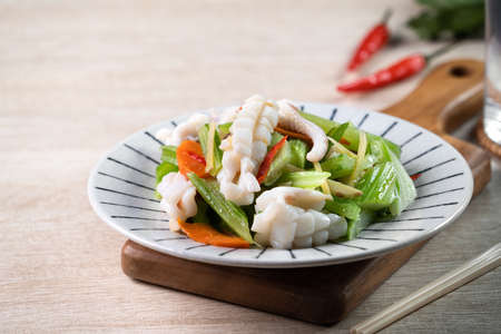 Stir-fried neritic squid with celery. Delicious homemade seafood with vegetable meal on wooden dining table background.の写真素材