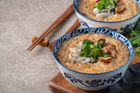 Homemade delicious oyster and large intestine vermicelli thin noodles in a bowl on dark wooden table background.の写真素材