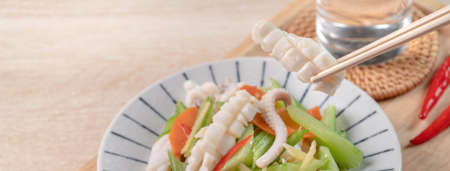 Stir-fried neritic squid with celery. Delicious homemade seafood with vegetable meal on wooden dining table background.の写真素材