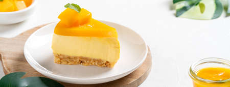 Delicious glazed mango no baked cheese cake with fresh diced mango pulp topping in a plate for serving on bright table background.の写真素材