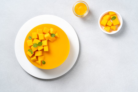 Delicious glazed mango no baked cheese cake with fresh diced mango pulp topping in a plate for serving on bright table background.の写真素材