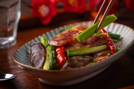 Delicious spicy homemade stir-fried Chinese smoked sausage with asparagus on dark wooden table for meal.の写真素材