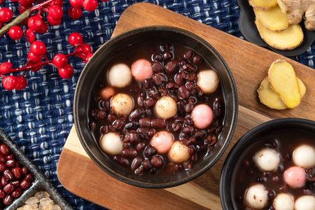 Traditional sweet red bean dessert soup with glutinous rice balls tangyuan in a black bowl on wooden...