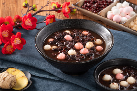 Traditional sweet red bean dessert soup with glutinous rice balls tangyuan in a black bowl on wooden...
