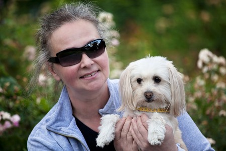 Middleaged woman holdiong her small dog and smiling at the cmaera.