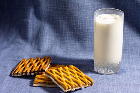 photo of a glass of milk on a blue background - with openwork puff pastry cookies with white...