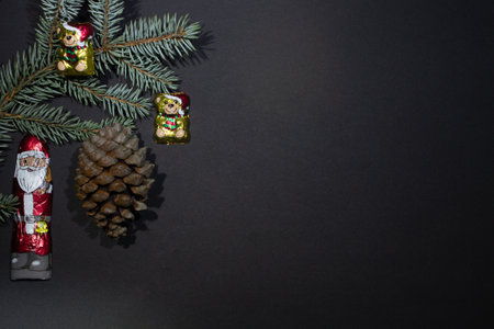Chocolate Christmas toys - santa claus and a bear on a christmas tree with a fir cone on a black background and empty space and a fir branchの写真素材