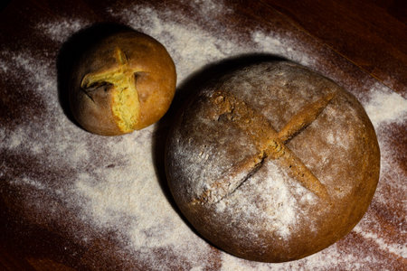 top view - two freshly baked round loaves on a dark wooden background with scattered flour