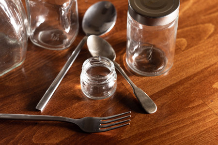 empty glass jars with two spoons and a fork on a dark wooden backgroundの写真素材