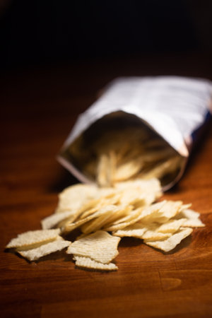 scattered ribbed potato chips from a pack on a dark wooden table with a blurred backgroundの写真素材