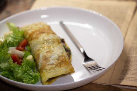 ruddy appetizing pancake with tuna and salad on a white ceramic plate with a fork against the background of an old newspaper close-upの写真素材
