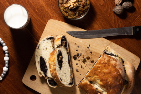 flat lay sliced on a bamboo wooden cutting board with a knife and a glass of milk on a dark wooden table with a bowl of raisin - nuts and a white Christmas tree toy - top viewの写真素材