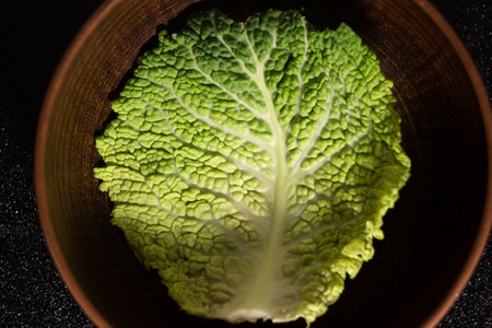 Close up - leaf of savoy cabbage in a round clay bowl on a black background - top viewの写真素材