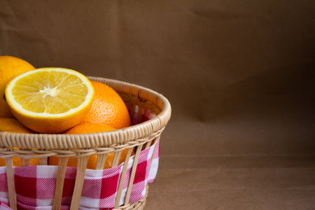 part of a wicker basket with ripe oranges and half an orange with a checkered cloth on a blurred light brown backgroundの写真素材