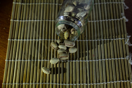 photo pistachios spilled out of a glass jar onto a bamboo makisの写真素材