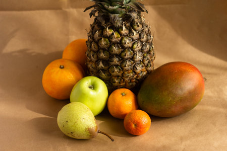 pineapple mango orange pear apple and tangerine - on a light brown background