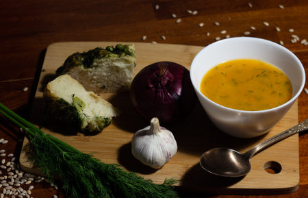 still life of pumpkin soup with cut slices of focaccia on a cutting board with onion and dill and garlic and scattered grits - on a dark wooden backgroundの写真素材