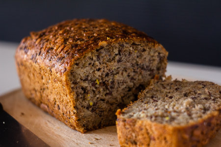 bread with different seeds sliced on a wooden cutting board - on a white table with a dark...