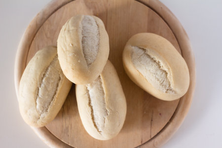 wheat buns for baking on a round wooden cutting board on a white background - top view