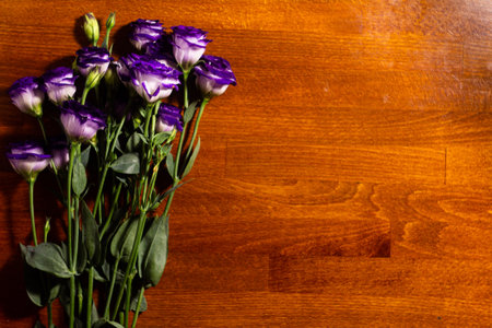 A bouquet of purple and white flowers rests on a smooth wooden table. The natural light highlights their colors, creating a lively atmosphere perfect for decoration or gifting.の写真素材