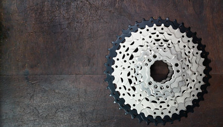 Detailed view of a metallic bicycle gear cog placed on a textured wooden surface displaying intricate design.の写真素材
