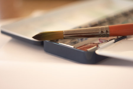 A painting brush is placed on a watercolor palette, ready for artistic use, in a gently lit creative space, evoking a sense of creativity and inspiration in an artistic environment.の写真素材