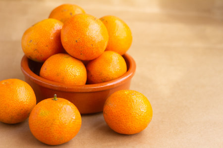 A collection of bright orange tangerines displayed in a rustic bowl on a brown surface, highlighting their natural vibrancy and healthy appeal.の写真素材